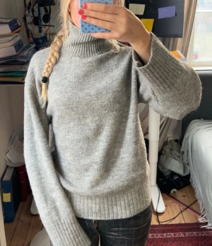 Grå stickad polotröja - Mysig grå polotröja med ribbade muddar och hög krage. Kragen kan antingen vara ”öppen” eller nervikt. Tröjan är stickad och har en relaxed passform med långa ärmar. Perfekt för kyliga dagar och enkel att matcha med jeans eller kjol.