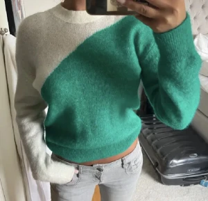 Other stores tröja som inte säljs längre  - Säljer en snygg stickad tröja i grönt och vitt med cool diagonal färgdelning. Tröjan har rund halsringning och långa ärmar. Perfekt för dig som gillar en chill och trendig look.