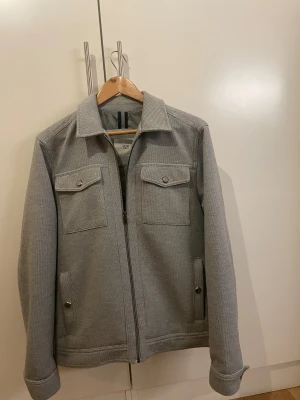 Grå overshirt  - Snygg grå overshirt från LCW med klassisk krage, två bröstfickor med knappar och dragkedja framtill. Jackan har en strukturerad yta och är tillverkad i ett bomullsliknande material. Perfekt för lager-på-lager och stilren look.