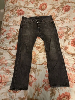 Levi's 501 svarta jeans W32 L30 - Svarta Levi's 501 jeans med klassisk rak passform och fem fickor. Jeansen har knappgylf och är tillverkade i slitstarkt bomullsjeansmaterial. Perfekt för dig som gillar tidlös stil och vill ha ett par jeans som funkar till allt.