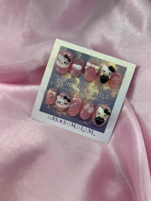 SweetKitty(S);ExtraShortOval  - Supergulliga handgjorda press-on naglar i rosa med glitter, 3D Hello Kitty-figurer, vita rosetter och svarta hjärtan. Naglarna har en extra kort oval form och kommer i S: 15 mm, 11,5 mm, 12 mm, 11 mm, 9 mm. Perfekt för dig som vill ha en söt och unik look med extra detaljer.