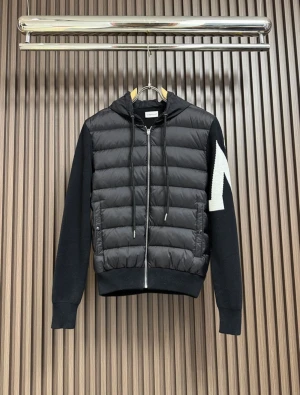 Svart pufferjacka med huva från Moncler - Svart pufferjacka från Moncler med stickade ärmar och huva. Jackan har dragkedja framtill, snörning i huvan och Moncler-logga på ärmen. Kroppen är quiltad och i glansigt material medan ärmarna är stickade i svart med vit detalj.