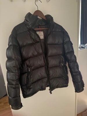 Svart Moncler pufferjacka herr - Säljer en svart pufferjacka från Moncler med hög krage och två dragkedjeförsedda fickor. Jackan har en glansig finish och klassisk Moncler-logga på insidan. Perfekt för kalla dagar och riktigt snygg streetstil.