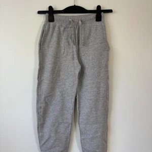 Grå mjukisbyxor - 134 Storlek  - Snygga grå mjukisbyxor från R i storlek 134. Byxorna har ribbad midja med snörning, muddar vid bensluten och mjukt material som känns skönt mot huden. 