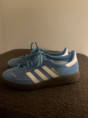 Adidas Spezial blå sneakers - Säljer ett par Adidas Spezial sneakers i ljusblå mocka med vita detaljer och klassiska tre ränder på sidan. Använda två gånger. Så som nya!!!