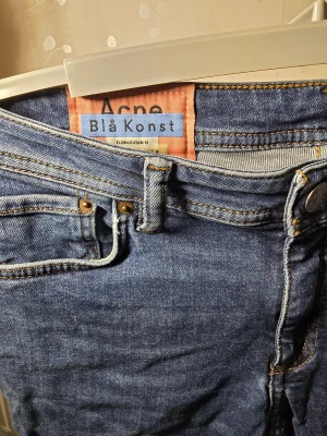 Blå Acne Blå Konst jeans - Snygga blå jeans från Acne Blå Konst med klassisk femficksdesign och gul kontrastsöm. Modellen har rak passform och normal midja, tillverkade i slitstarkt bomullsjeansmaterial. Perfekta för dig som gillar stilrena och tidlösa jeans. W28 L32