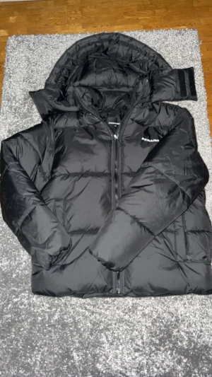 Svart pufferjacka från Pegador XS - Säljer en svart pufferjacka från Pegador i storlek XS. Jackan har huva, hög krage och dragkedja framtill. Den är vadderad och har en clean look med Pegador-logga på bröstet. Perfekt för kalla dagar när du vill hålla stilen.Passar dig som har S