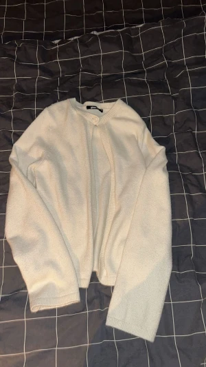 Vit kofta från Gina Tricot - Mysig vit kofta från Gina Tricot med rund hals och en knapp framtill. Koftan har långärmade ärmar och är tillverkad i ett mjukt stickat material som känns skönt mot huden. Perfekt att slänga på sig när det är lite kyligt ute.