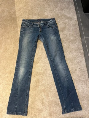 Blå bootcut jeans från Bik Bok - Snygga blå jeans från Bik Bok i bootcut-modell med klassisk femficksdesign och slitna detaljer på bakfickorna. Jeansen har låg midja och är i st M men jag skulle säga att de passar någon med st 36