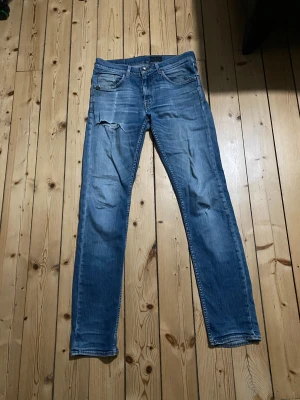 Blå jeansbyxor från Tiger of Sweden, 32/34 - Snygga blå jeansbyxor från Tiger of Sweden i klassisk femficksmodell. Byxorna har en slim passform med raka ben och slitningar på framsidan för en cool look. Tillverkade i jeansmaterial med kontrastsömmar och knappgylf. Perfekt för dig som gillar en avslappnad stil.