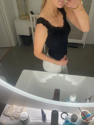 Svart linnetopp med spetskant - Säljer en svart linnetopp med breda axelband och snygg spetskant runt halsringningen. Toppen är figurnära och har en enkel, stilren design som är lätt att matcha. Perfekt för dig som gillar en feminin och clean look.