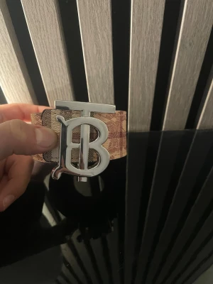 Burberry bälte med TB-spänne - Säljer ett Burberry bälte med stort TB-monogram i silverfärgad metall. Bältet har klassiskt rutigt mönster i beige, brunt och svart samt en variant i svart och grått. Perfekt accessoar för att lyfta din outfit med en lyxig touch.