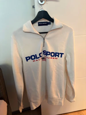 Vit Polo Sport half zip tröja - Säljer en vit Polo Sport Ralph Lauren tröja som inte kommer till användning. Klassisk och sportig look. Hör av dig om du har några funderingar!