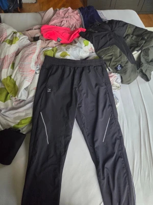 Svarta träningsbyxor från SOC, strl L - Svarta träningsbyxor från SOC med elastisk midja och smal passform. Byxorna har reflekterande detaljer längs benen och dragkedja vid benslut. Materialet är syntet med insida i fleece för extra komfort. Perfekta för löpning eller utomhusträning.