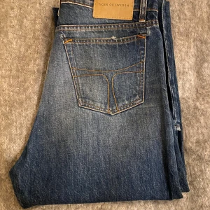 Blå jeans från Tiger of Sweden - Snygga blå jeans från Tiger of Sweden med klassisk femficksdesign och raka ben. Jeansen har kontrastsömmar och en läderpatch med logga bak i midjan. Materialet är slitstarkt denim och passformen är normal med straight legs.