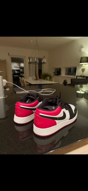 Nike Air Jordan 1 Low svart/röd/vit - Nike Air Jordan 1 Low sneakers med klassisk design i svart, rött och vitt. Skorna har snörning, rund tå och platt sula. Tillverkade i skinn med detaljer i syntet. Swoosh-logga på sidan och Air Jordan-märke på hälen. 