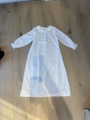 Vitt lucia linne med spetskrage H&M strl 110/116 - Supersöt vitt lucia linne från H&M med lång ärm och rundad spetskrage. Klänningen har diskreta rynkdetaljer vid bysten och ärmarna avslutas med elastisk kant och liten spets. Tillverkad i mjuk bomull, perfekt för en klassisk look. 