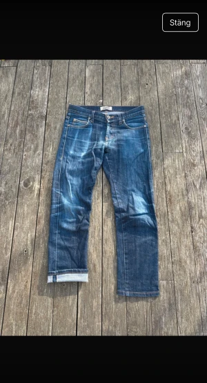 selvedge jeans från Naked & Famous - Snygga blå jeans från Naked & Famous med klassisk femficksdesign och tydliga slitningar för en cool, använd look. Inga hål. Jeansen har raka ben och ganska slim passform, med kontrastsömmar och läderpatch bak i midjan. Perfekta för dig som gillar stilrena denim. De är selvedge