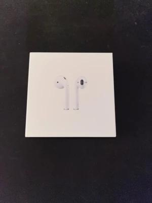 Apple AirPods 2 - Säljer ett par Apple AirPods 2 i originalförpackning. Trådlösa hörlurar med laddningsetui, kompatibla med iPhone och andra enheter. Produkten ser ut att vara i gott skick utan synliga skador eller slitage. Perfekt för musik, samtal och smidig anslutning.