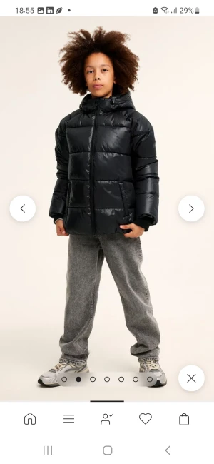 Svart pufferjacka med huva - Svart pufferjacka med glansig finish och huva. Jackan har breda, quiltade sektioner och dragkedja framtill. Perfekt för kalla dagar och har en clean, modern look. Passformen är normal och jackan är fodrad för extra värme. Endast använd en vinter.