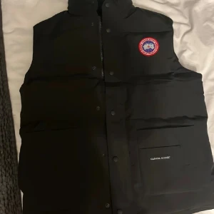 Canada goose väst- Mycket bra skick - Klassisk och tidlös Canada Goose-väst i svart. Västen är i mycket bra skick, sparsamt använd och väl omhändertagen. Perfekt som ett lättare ytterplagg under höst/vår eller att ha som ett extra lager under jackan på vintern. 	•	Färg: Svart 	•	Storlek: L 	•	Mycket bra skick – inga skador, fläckar eller slitage                                                                     Nypris ca:7499kr   