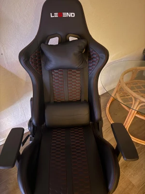 Legend Gaming Chair - Snygg och ergonomisk gamingstol från Legend med svart och röd design, justerbara armstöd, nack- och ryggkudde. Stolen ser ut att vara i mycket gott skick utan synligt slitage, perfekt för långa spelsessioner eller kontorsarbete.