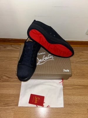Christian Louboutin mörkblå loubs  - Snygga svarta sneakers från Christian Louboutin med klassisk röd sula och rund tå. Skorna har snörning och är tillverkade i mocka med stilrena detaljer. Perfekt för dig som vill ha en exklusiv och modern look med lyxig känsla.