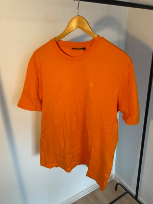 Orange t-shirt från J.Lindeberg -storlek Large - Snygg orange t-shirt från J.Lindeberg i storlek L. Tillverkad i mjuk bomull med rund hals och korta ärmar. Diskret logga på bröstet. Perfekt för dig som gillar färgstarka och stilrena plagg.