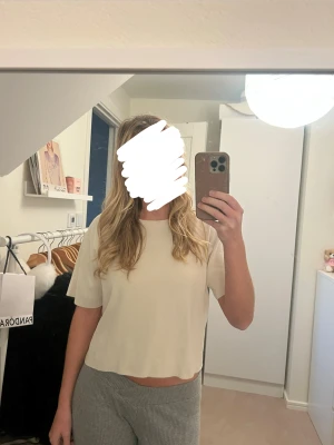 Beige croppad topp med kort ärm - Säljer en  beige croppad topp med korta ärmar. Toppen har en enkel och avslappnad passform, perfekt för dig som gillar minimalistisk stil.