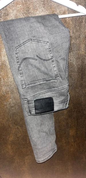 Grå skinny jeans från Jack & Jones - Snygga grå jeans från Jack & Jones med slim passform och klassisk femficksdesign. Jeansen har en mörkgrå tvätt med slitningar och detaljerade sömmar. Materialet är mjukt jeans-tyg med stretch för extra komfort. Perfekt för dig som gillar en stil ren look. 