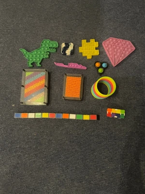 Fidget och sensoriska leksaker, mixad samling - Stor samling fidget- och sensoriska leksaker: pop-its, regnbågsfärgad slinky, pin art, snake puzzle, infinity cube och fler. Perfekt för stresslindring och koncentration. Alla delar i gott skick, inga synliga defekter eller slitage.