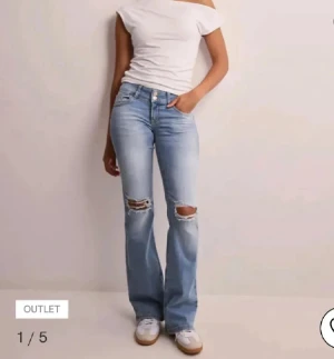 Ljusblå bootcut jeans från Nelly - Säljer ett par ljusblå bootcut jeans från Nelly med slitna detaljer vid knäna. Jeansen har klassisk femficksdesign, bälteshällor och dragkedja med knapp framtill. Perfekta för en avslappnad och trendig look.