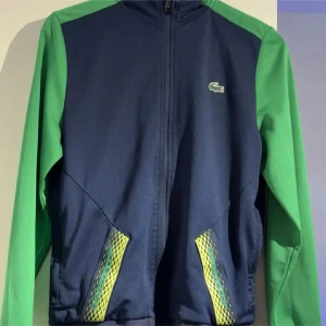 Lacoste Sport blå-grön ziptröja S - Snygg ziptröja från Lacoste Sport i marinblått med gröna ärmar och detaljer i gult vid fickorna. Klassisk krokodillogo på bröstet, långärmad och med dragkedja hela vägen. Perfekt för träning eller chill. Classic fit och sportig vibe. Säljs inte längre på Lacostes hemsida eller butik😁