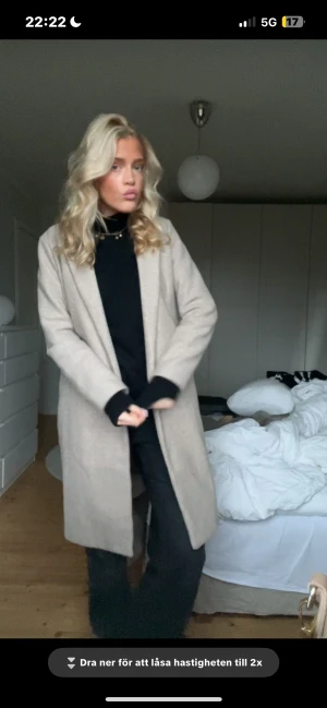 Beige kappa med lång ärm - Snygg beige kappa med rak passform och lång ärm. Jackan har en stilren design utan synliga knappar eller dragkedja, och är tillverkad i ett mjukt material som ger en clean look. Perfekt för dig som gillar minimalistisk stil.
