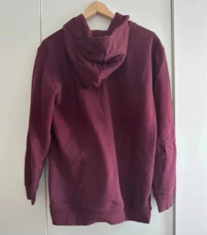 Vinröd Adidas hoodie med logga - Säljer en vinröd hoodie från Adidas med klassiska trefoil-loggan i vitt på framsidan. Tröjan har huva med snörning, magficka och långa ärmar. Perfekt för både vardag och chill dagar