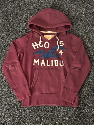 Vinröd hoodie Hollister Malibu S (sällsynt) - Säljer nu denna sjukt eftertraktade hoodien ifrån hollister. Skick 8/10, Rikigt snygg och passar perfekt nu till hösten. Obs kan gå ner i pris vid snabb affär! Slitage design 