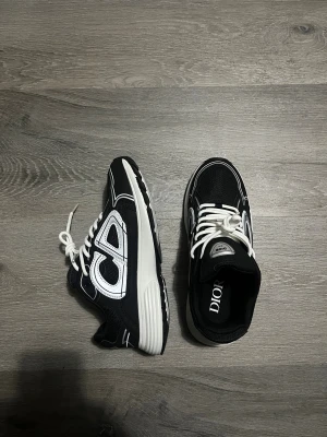 Svarta Dior B30 sneakers - Säljer ett par svarta och vita Dior B30 sneakers med chunky sula och tydlig Dior-logga på sidan. Skorna har snörning, mesh och syntetdetaljer samt en sportig vibe. Perfekta för dig som vill sticka ut med exklusiva och trendiga sneakers.