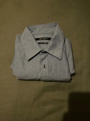 Blå slim fit skjorta Tiger of Sweden - Snygg blå skjorta från Tiger of Sweden med diskret prickigt mönster. Skjortan är slim fit med stretch för extra komfort och har klassisk krage samt knappar framtill. Perfekt för dig som gillar stilrena detaljer och en modern passform.
