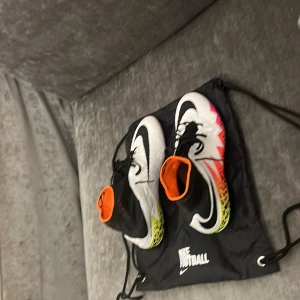 Nike Hypervenom fotbollsskor - Säljer ett par Nike Hypervenom fotbollsskor med högt skaft och snörning. Skorna är vita med svarta detaljer, orange insida och färgglad sula i gul, orange och rosa med grafiskt mönster. Ovandelen är syntetmaterial och designen är riktigt sportig och modern.