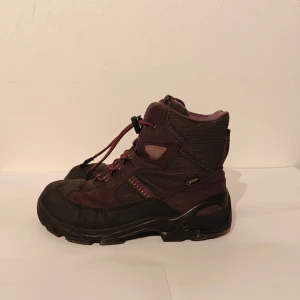 Ecco kängor  - Säljer ett par mörklila kängor från Ecco i storlek 34. Skorna har snörning med snabbspänne, robust platt sula och detaljer i mesh och mocka. Gore-Tex-membran för extra skydd mot väta. Perfekt för höst och vinter när du vill ha både stil och funktion.