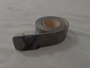 Louis Vuitton monogram skärp i skinn - Säljer ett snyggt Louis Vuitton bälte i brunt skinn med klassiskt monogrammönster och svart metallspänne med LV-logga. Insidan är ljusbeige med vita sömmar. Perfekt accessoar för att lyfta din outfit med exklusiv känsla.