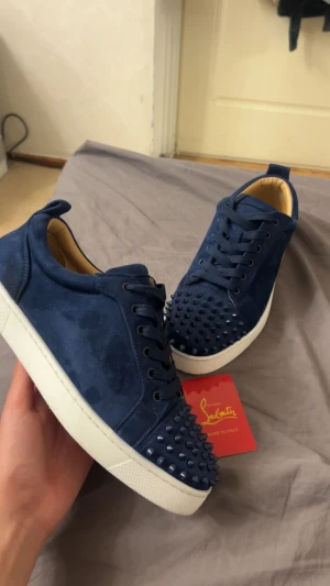 Blå sneakers med nitar - Snyggas skor i mocka med coola ton-i-ton nitar över tån. Skorna har vita platta sulor, rund tå och klassisk snörning. Insidan är beige och mjukt vadderad för extra komfort. Perfekt för dig som vill sticka ut med exklusiv streetstyle.