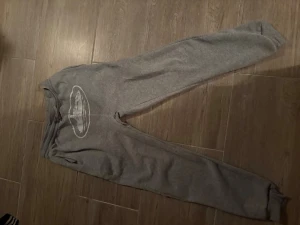 Grå mjukisbyxor med tryck - Grå mjukisbyxor med resår och snörning i midjan samt ett vitt tryck med motiv på ena benet. Byxorna har ribbade muddar vid bensluten och är tillverkade i mjukt bomullsmaterial. Perfekta för chill eller träning. Passar bra för dig som är 170-175cm