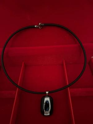 Halsband med dikroiskt glas - Unikt halsband med svart rektangulär hängare, dekorerad med en silvrig struktur och glittrande blå inslag i mitten. Hängaren sitter på ett svart rundat band med silverfäste. Perfekt för dig som gillar coola och moderna smycken.