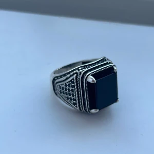 Silverring med svart sten och mönster - Snygg äkta silverring (925) med en stor, rektangulär svart sten i centrum. Ringen har detaljerade, graverade mönster längs sidorna och runt stenen, vilket ger den en unik och cool vibe. Perfekt för dig som gillar statement-smycken med lite edge.