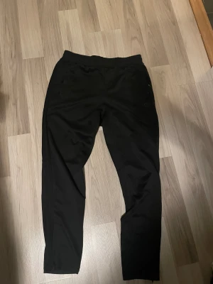 Svarta mjukisbyxor från OTP, stl S - Svarta mjukisbyxor från OTP i storlek S. Byxorna har elastisk midja och raka ben, perfekt för chill eller träning. Tillverkade i mjukt och bekvämt material med diskret logga på ena benet. Snygg och enkel design som funkar till det mesta.