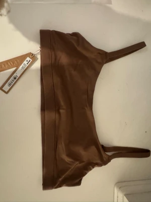 Brun linnetopp från Skims - Säljer en helt ny brun linnetopp från Skims med tunna, justerbara axelband och enkel, stilren design. Toppen är gjord i ett mjukt och stretchigt material som sitter skönt mot kroppen. Perfekt att bära under skjortor eller som den är. 