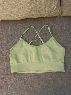 Träningstopp - Bilderna visar ett grönt sportlinne med korsade axelband, tillverkat av polyamid och elastan. Nästan som helt ny