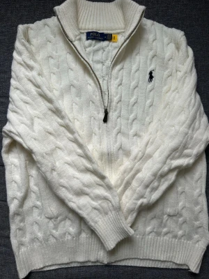 Ralph Lauren tröja - Vit kabelstickad tröja från Polo Ralph Lauren i storlek M. Tröjan är full zip, ribbade muddar och lång ärm. Har även qr kod som autentisering för plagget.                                         Nypris: 3500kr