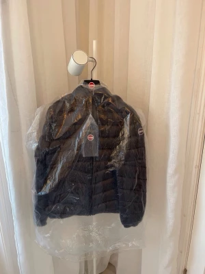 Svart Colmar pufferjacka med huva - Säljer en svart helt ny pufferjacka med etikett från Colmar Originals med huva och dragkedja framtill. Jackan har Colmar-logga på ärmen och två snedställda fickor. Materialet är glansigt och lätt, perfekt för kyliga dagar. Ny pris ligger på 3950 kr. Snygg och enkel design som funkar till allt både i vardagen eller vid finare tillfällen. Bara höra av sig vid funderingar, pris går att diskutera.